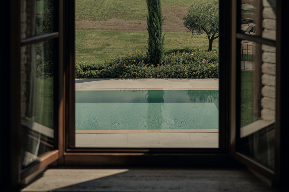 Vue depuis une fenêtre ouverte sur la piscine et le jardin d'une propriété